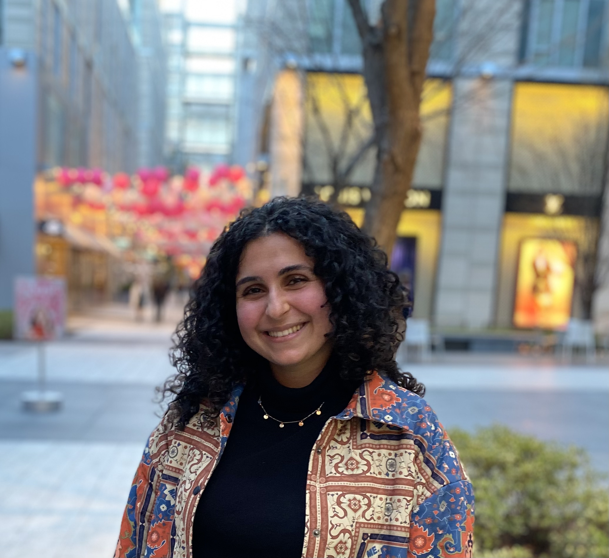 Pegah wearing a colorful jacket in front of a blurred urban background